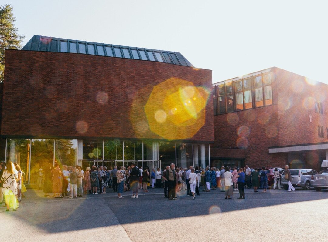 Konserttiyleisöä Jyväskylän yliopiston punatiilisen päärakennuksen edessä aurinkoisena kesäiltana.